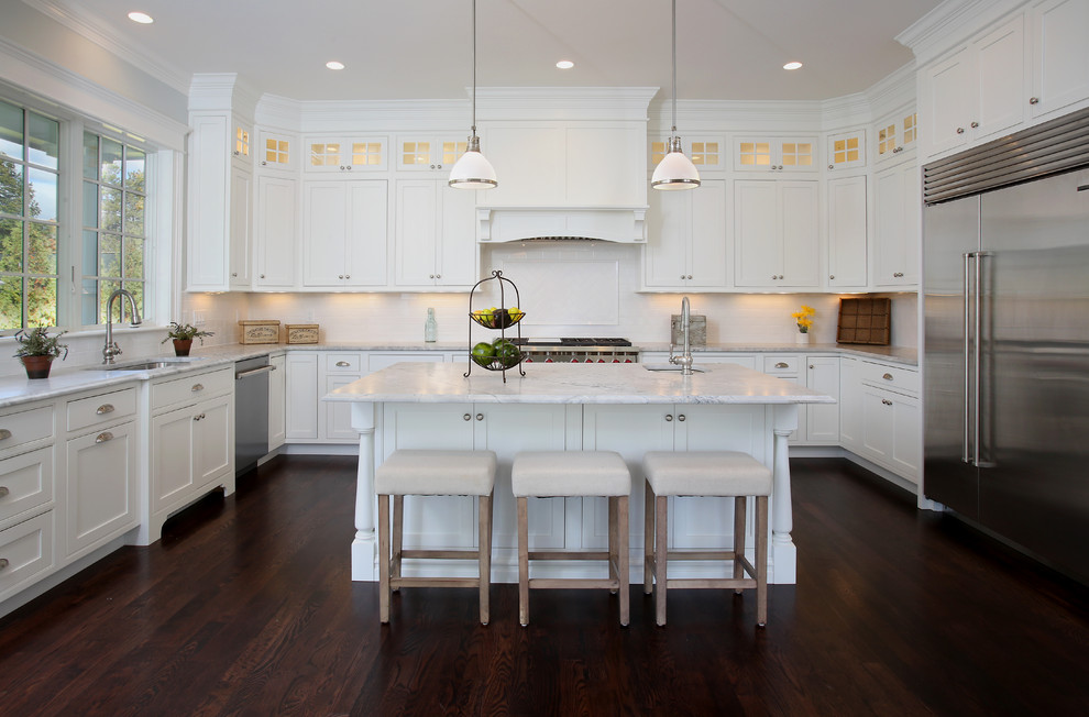 Photo of a traditional u-shaped kitchen in Boston with an undermount sink, shaker cabinets, white cabinets, white splashback, stainless steel appliances, dark hardwood floors and with island.