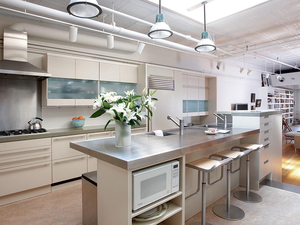 Photo of an industrial open plan kitchen in New York with with island, flat-panel cabinets, beige cabinets, stainless steel benchtops, metallic splashback and panelled appliances.