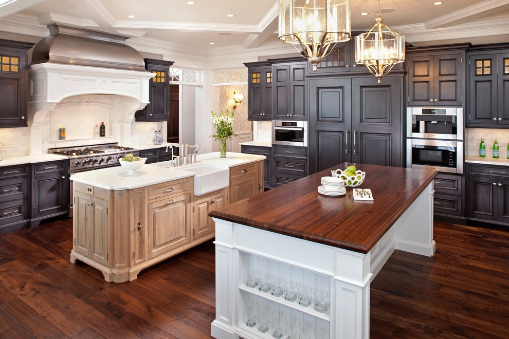 This is an example of a transitional kitchen in Minneapolis with a farmhouse sink, raised-panel cabinets, black cabinets, wood benchtops, white splashback and panelled appliances.