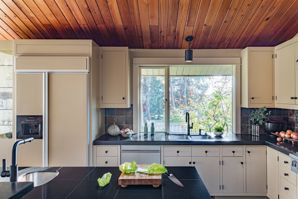 Photo of a large midcentury l-shaped eat-in kitchen in Portland with a double-bowl sink, flat-panel cabinets, beige cabinets, granite benchtops, multi-coloured splashback, slate splashback, stainless steel appliances, slate floors, with island, brown floor and black benchtop.