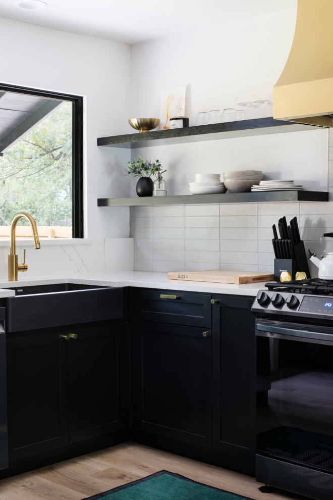 Open concept kitchen - mid-sized transitional u-shaped medium tone wood floor and brown floor open concept kitchen idea in Austin with a farmhouse sink, shaker cabinets, black cabinets, quartz countertops, white backsplash, porcelain backsplash, stainless steel appliances, a peninsula and white countertops