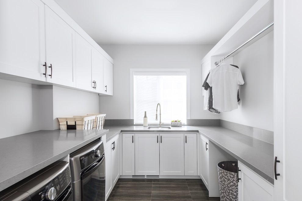 Mid-sized contemporary single-wall utility room in Toronto with an undermount sink, shaker cabinets, white cabinets, solid surface benchtops, porcelain floors, a side-by-side washer and dryer, brown floor, grey benchtop and white walls.