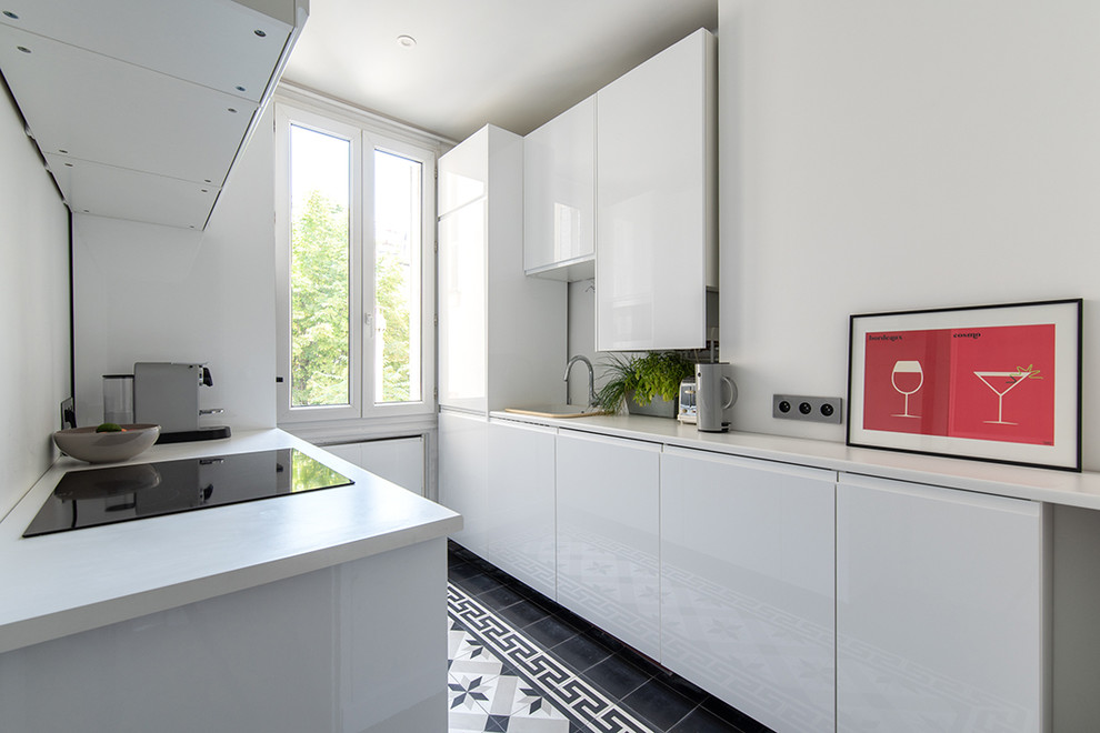 Small contemporary galley separate kitchen in Paris with a drop-in sink, flat-panel cabinets, white cabinets, white splashback, stainless steel appliances, cement tiles, no island, black floor and white benchtop.