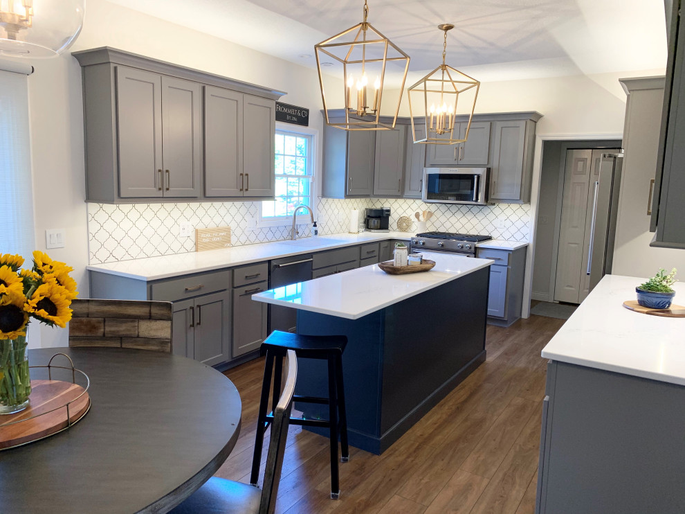 This is an example of a large transitional galley eat-in kitchen in Other with a farmhouse sink, recessed-panel cabinets, grey cabinets, quartz benchtops, white splashback, mosaic tile splashback, stainless steel appliances, medium hardwood floors, with island, brown floor and white benchtop.
