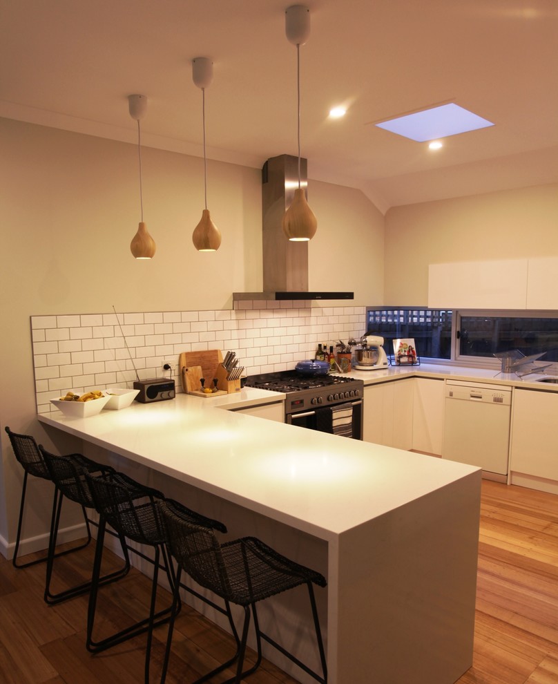 Inspiration for a contemporary u-shaped eat-in kitchen in Melbourne with an undermount sink, white splashback, subway tile splashback, stainless steel appliances, light hardwood floors, no island and white cabinets.