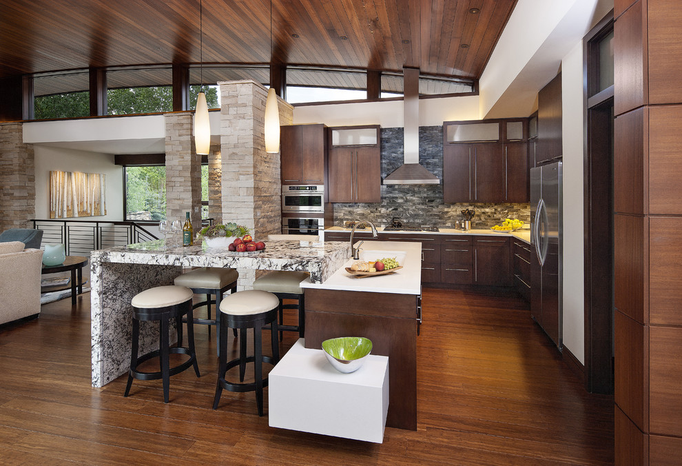 This is an example of a contemporary l-shaped open plan kitchen in Denver with an undermount sink, flat-panel cabinets, dark wood cabinets, quartzite benchtops, grey splashback, glass tile splashback, stainless steel appliances, bamboo floors and multiple islands.