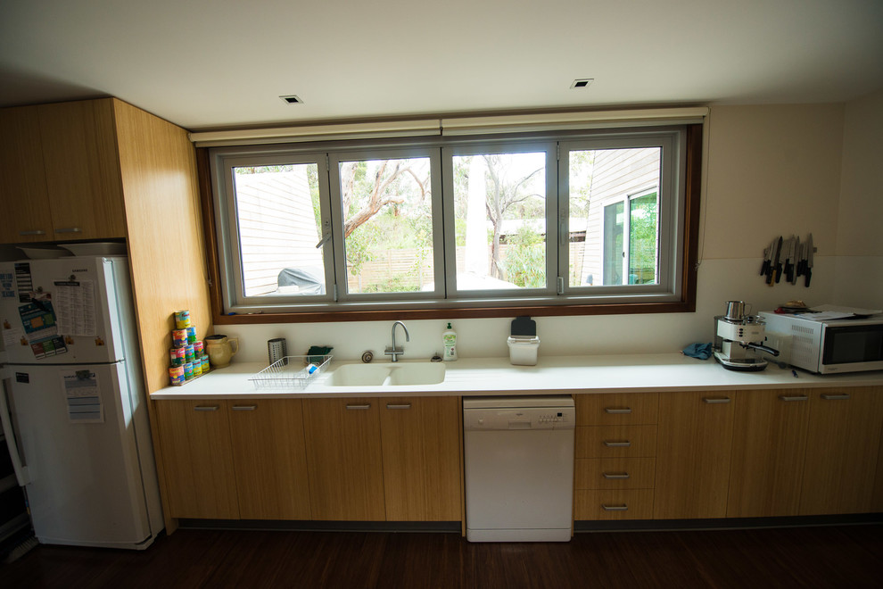 Design ideas for a large contemporary galley kitchen pantry in Melbourne with an integrated sink, flat-panel cabinets, light wood cabinets, solid surface benchtops, white splashback, glass sheet splashback, stainless steel appliances, bamboo floors and no island.