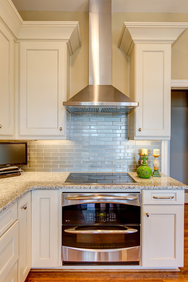 Example of a mid-sized transitional l-shaped light wood floor open concept kitchen design in Birmingham with a single-bowl sink, flat-panel cabinets, white cabinets, granite countertops, green backsplash, glass tile backsplash, stainless steel appliances and an island