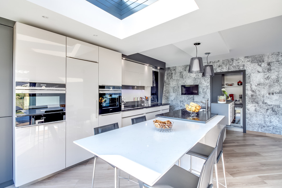 Design ideas for a mid-sized contemporary galley eat-in kitchen in Angers with flat-panel cabinets, white cabinets, stainless steel benchtops, white splashback, white appliances, light hardwood floors and with island.