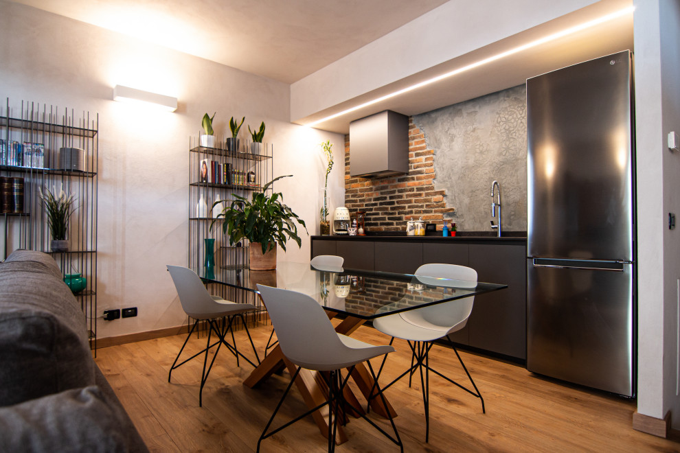 This is an example of a small urban open plan dining room in Milan with laminate floors and brick walls.