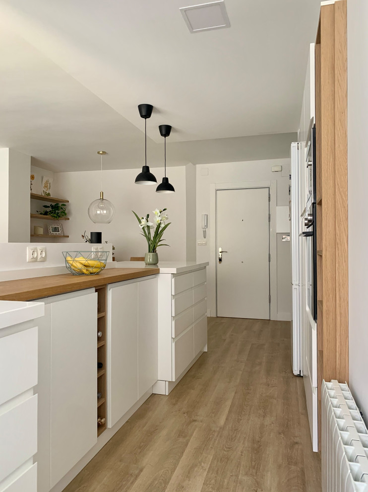 Skandinavisk inredning av ett litet vit vitt kök med öppen planlösning, med en enkel diskho, vita skåp, vitt stänkskydd, mellanmörkt trägolv, en halv köksö och beiget golv