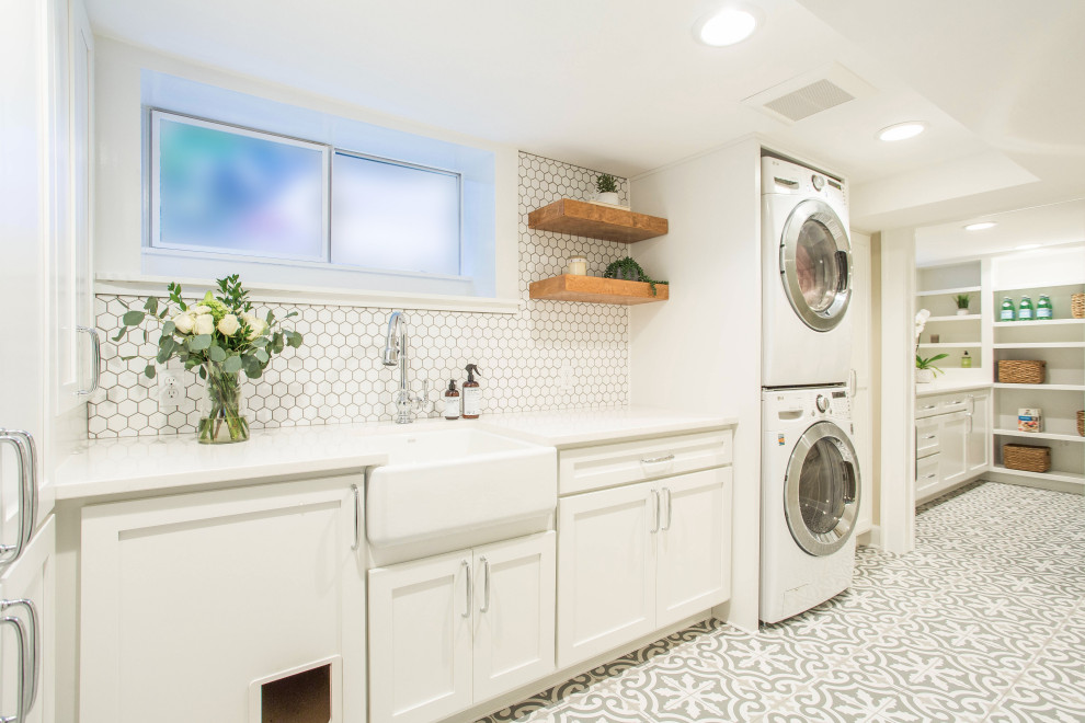 Design ideas for a mid-sized country galley dedicated laundry room in Seattle with a farmhouse sink, shaker cabinets, white cabinets, quartz benchtops, white walls, porcelain floors, a stacked washer and dryer, grey floor and white benchtop.