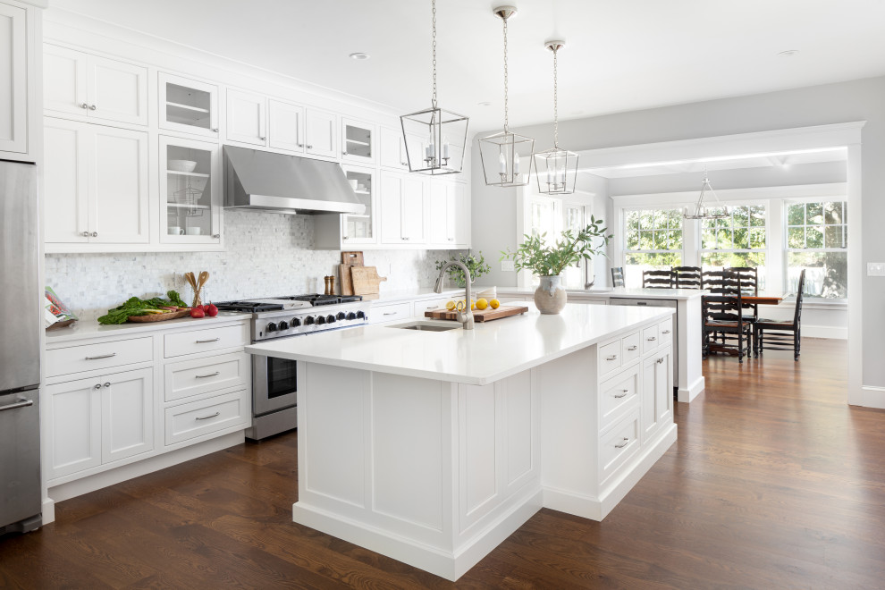This is an example of a traditional l-shaped eat-in kitchen in Providence with an undermount sink, glass-front cabinets, white cabinets, multi-coloured splashback, stainless steel appliances, medium hardwood floors, with island and white benchtop.