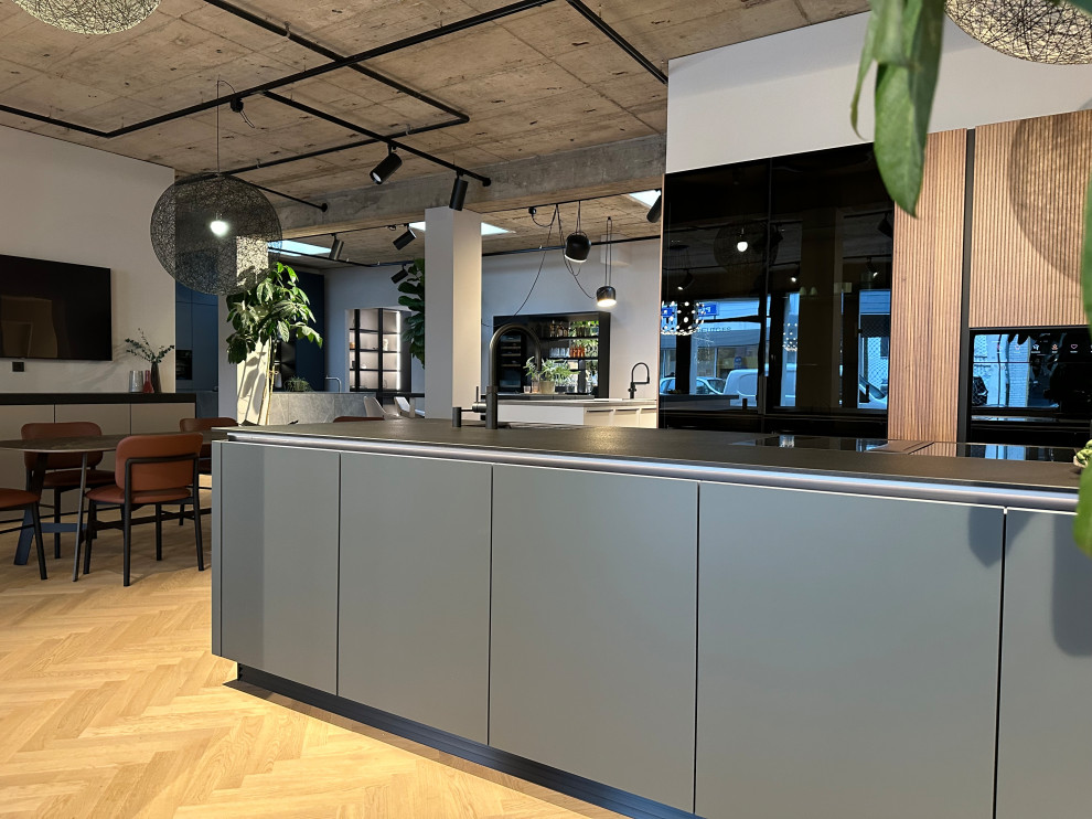 Küche mit Einbauwaschbecken, Glasfronten, grünen Schränken, Granit-Arbeitsplatte, schwarzen Elektrogeräten, hellem Holzboden, Kücheninsel und schwarzer Arbeitsplatte in Dusseldorf