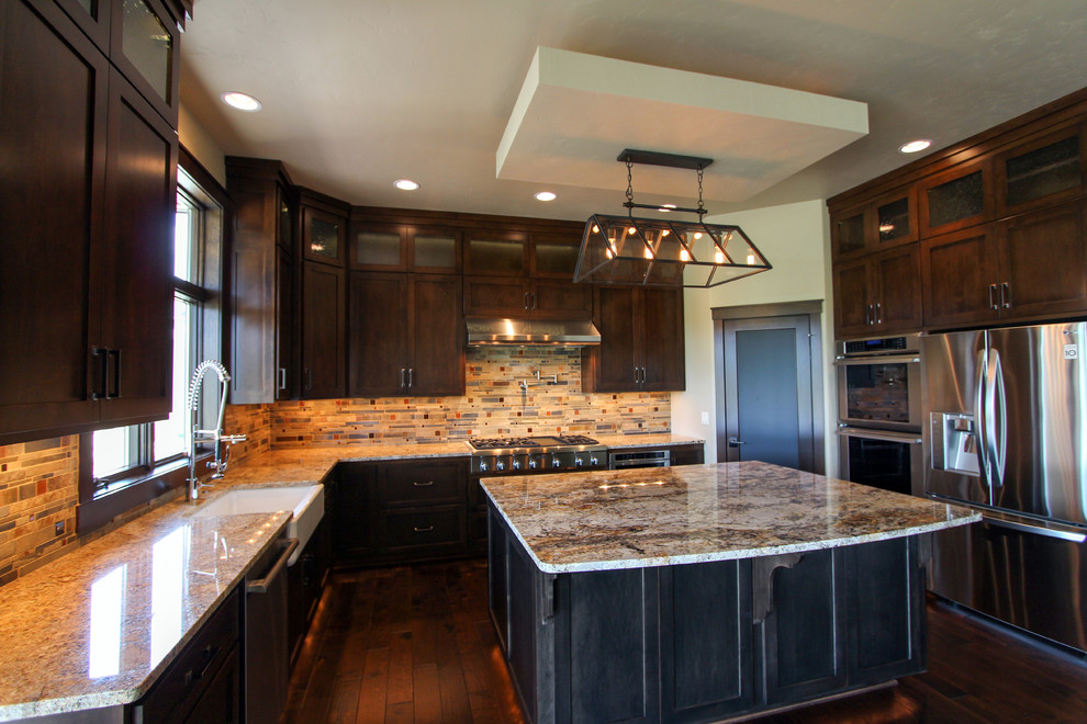 Transitional u-shaped eat-in kitchen in Milwaukee with a farmhouse sink, shaker cabinets, dark wood cabinets, granite benchtops, multi-coloured splashback, stainless steel appliances, dark hardwood floors and with island.