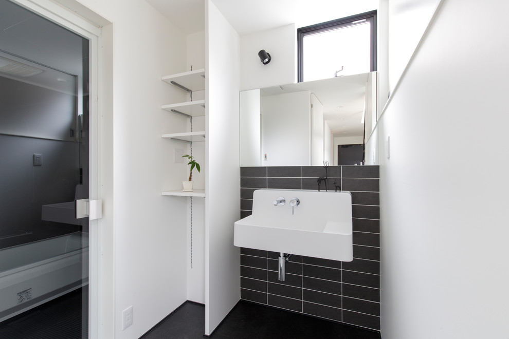 Modern powder room in Other with white walls, a wall-mount sink and black floor.