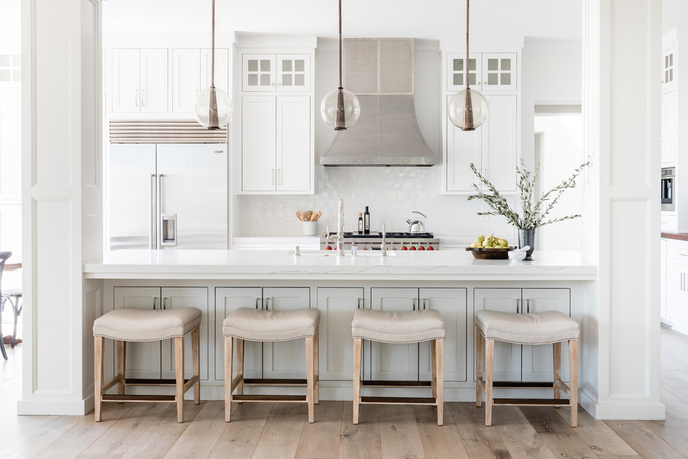 Example of a transitional medium tone wood floor and brown floor kitchen design in Sacramento with shaker cabinets, white cabinets, white backsplash, stainless steel appliances, an island and white countertops