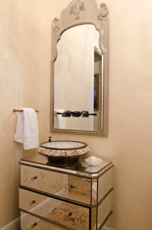 This is an example of a mid-sized traditional powder room in Austin with a vessel sink, furniture-like cabinets, glass benchtops, a two-piece toilet and beige walls.
