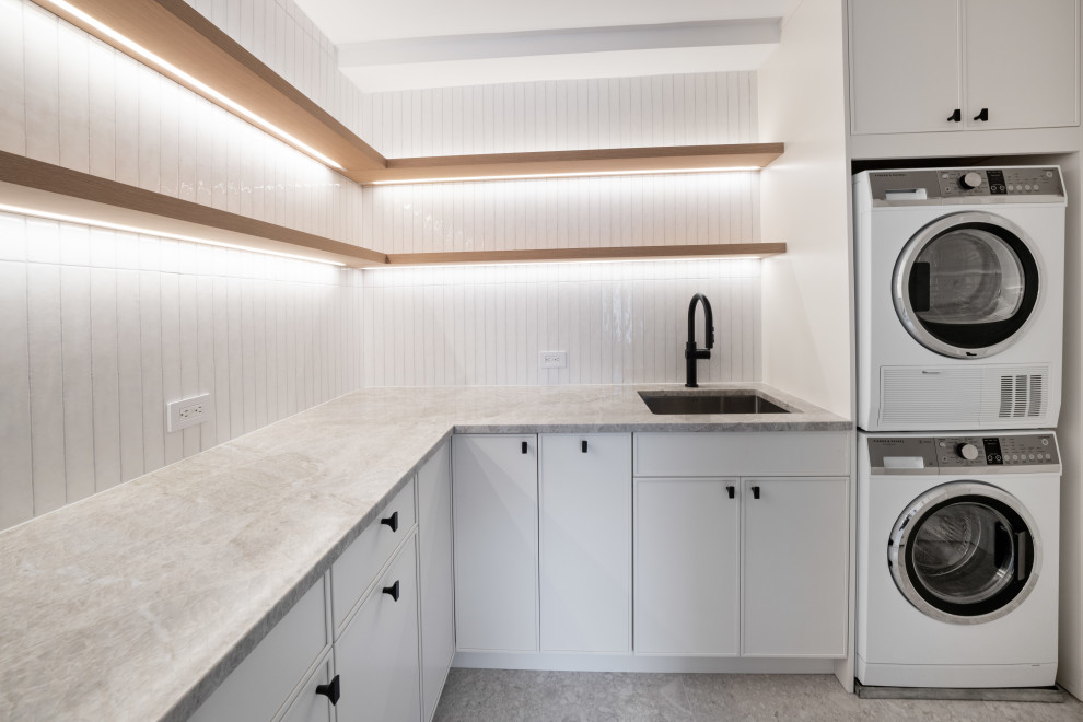 Inspiration for a medium sized modern utility room in New York with a submerged sink, shaker cabinets, white cabinets, quartz worktops, white splashback, ceramic splashback, white walls, porcelain flooring, a stacked washer and dryer and multi-coloured floors.