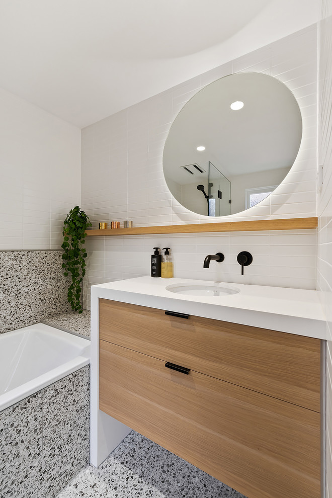 Design ideas for a small scandinavian master bathroom in Perth with flat-panel cabinets, light wood cabinets, a drop-in tub, a shower/bathtub combo, a one-piece toilet, white tile, porcelain tile, white walls, porcelain floors, an undermount sink, engineered quartz benchtops, grey floor, a hinged shower door and white benchtops.