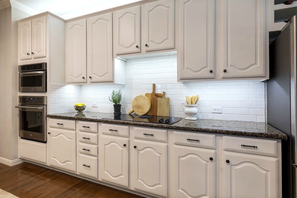 Inspiration for a large transitional galley medium tone wood floor open concept kitchen remodel in Dallas with an undermount sink, white cabinets, granite countertops, white backsplash, subway tile backsplash, stainless steel appliances and two islands