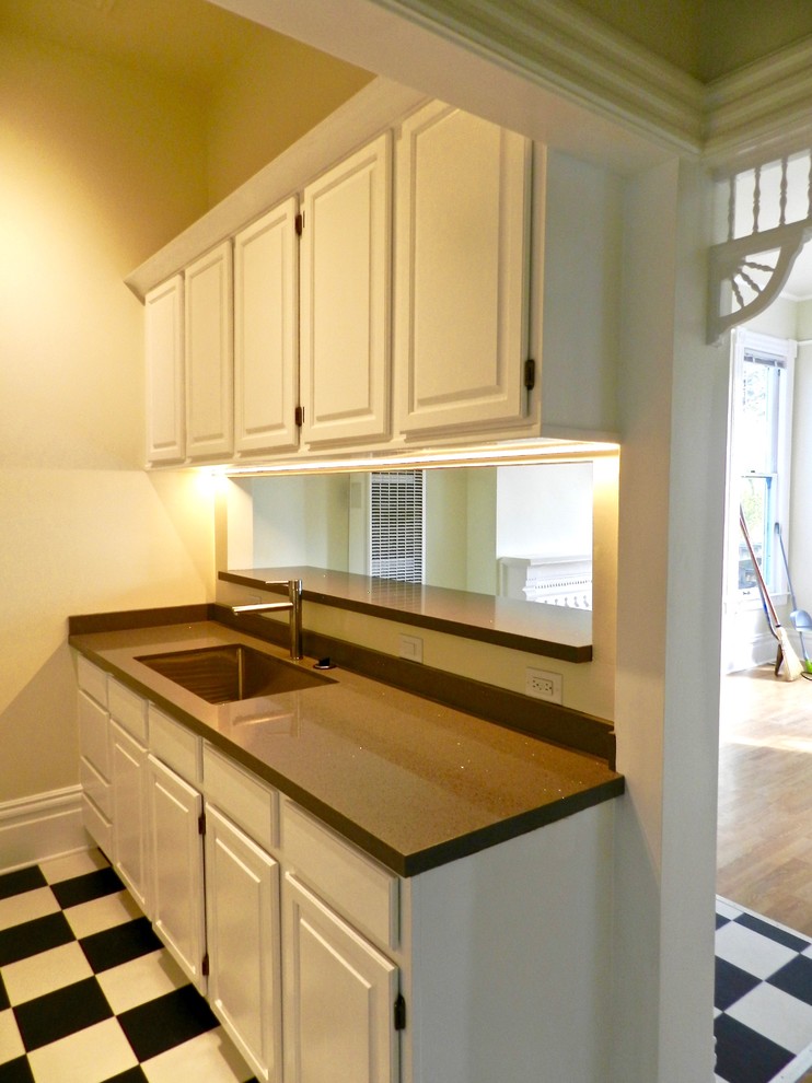 Photo of a small traditional galley eat-in kitchen in San Francisco with an undermount sink, raised-panel cabinets, white cabinets, grey splashback, stone slab splashback, white appliances, vinyl floors and no island.