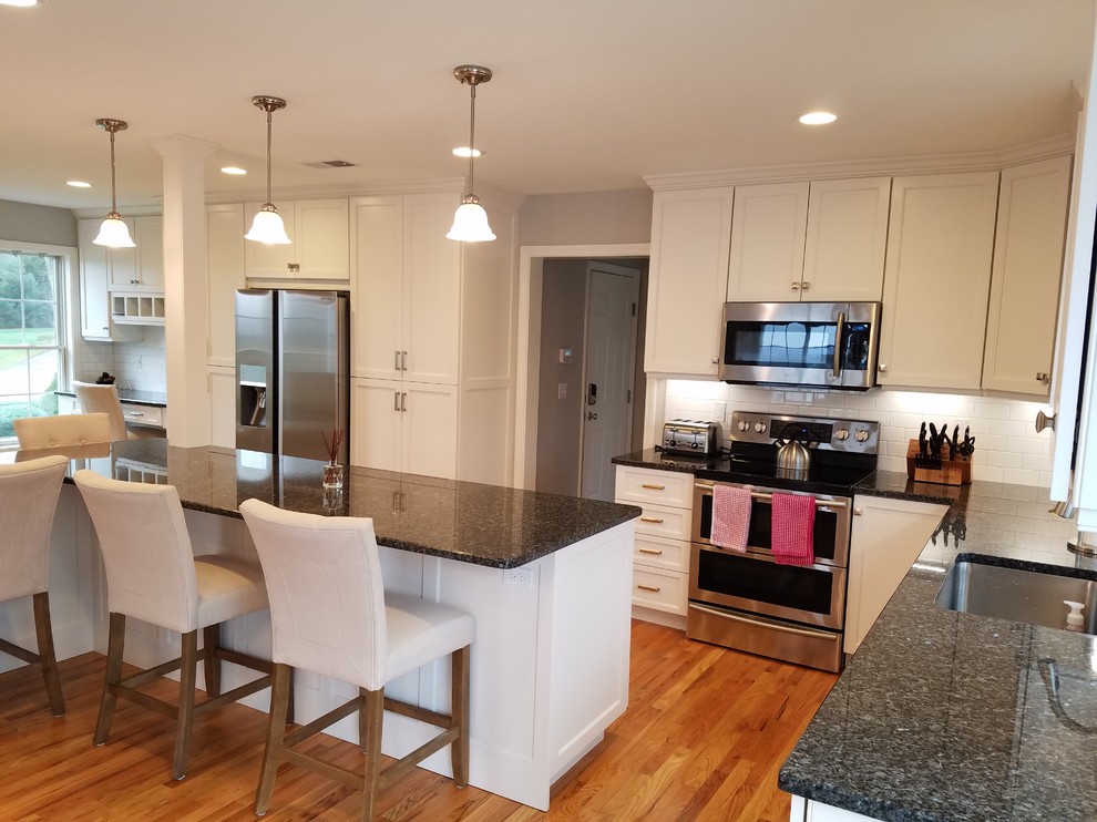 Inspiration for a large transitional l-shaped light wood floor and brown floor eat-in kitchen remodel with an undermount sink, shaker cabinets, white cabinets, granite countertops, white backsplash, subway tile backsplash, stainless steel appliances and an island