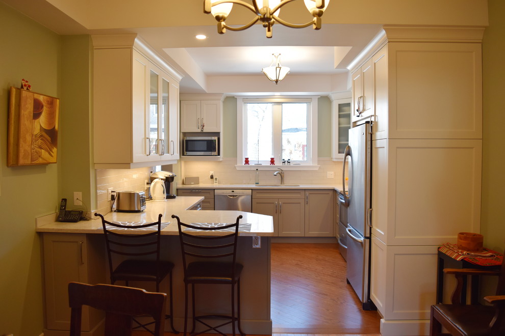 Mid-sized transitional l-shaped medium tone wood floor eat-in kitchen photo in Toronto with an undermount sink, shaker cabinets, white cabinets, quartz countertops, white backsplash, subway tile backsplash, stainless steel appliances and a peninsula