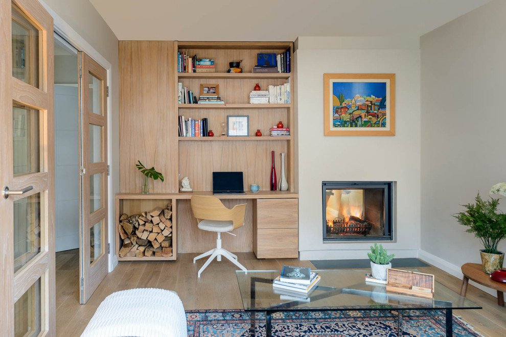 Inspiration för ett mellanstort minimalistiskt hemmabibliotek, med ljust trägolv, en dubbelsidig öppen spis och ett inbyggt skrivbord
