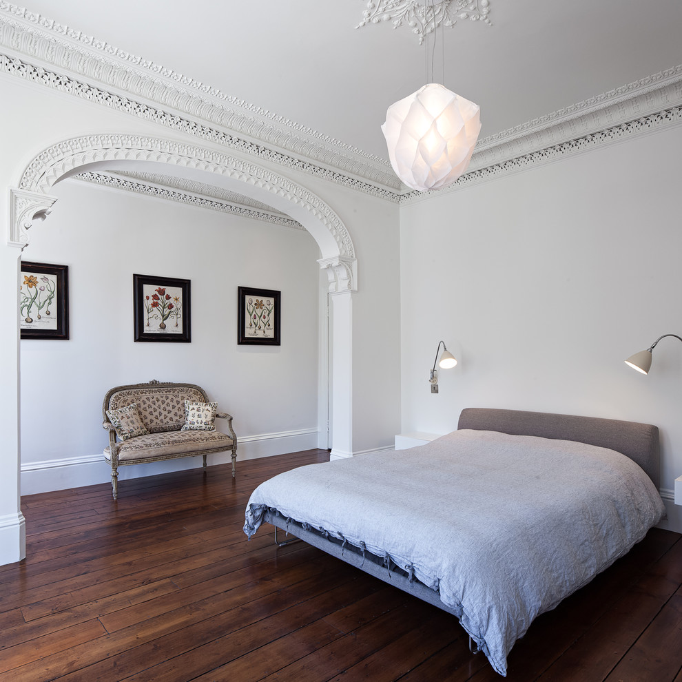 Large eclectic bedroom in London with white walls and dark hardwood floors.