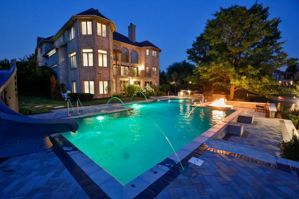 Ejemplo de piscina con tobogán alargada tradicional de tamaño medio a medida en patio trasero con adoquines de hormigón