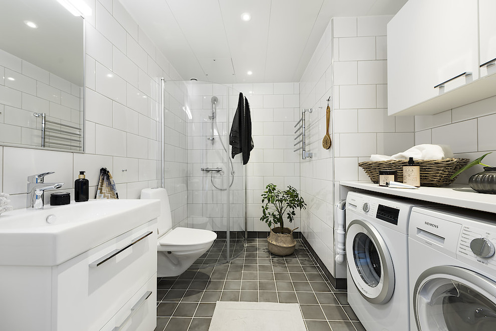 Photo of a scandinavian 3/4 bathroom in Other with flat-panel cabinets, white cabinets, a corner shower, a two-piece toilet, white tile, an integrated sink, grey floor, a hinged shower door, white benchtops and a laundry.