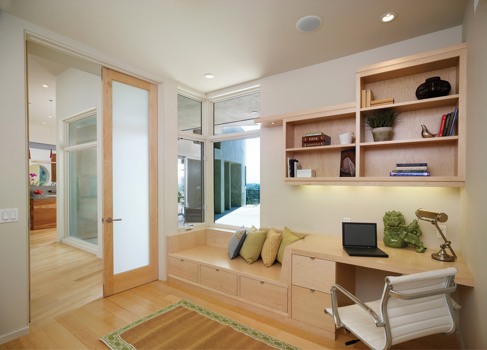 This is an example of a contemporary home office in Los Angeles with white walls, a built-in desk and light hardwood floors.