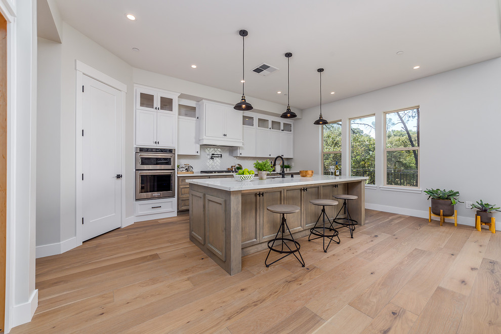 Mid-sized country l-shaped kitchen pantry in Sacramento with an integrated sink, flat-panel cabinets, medium wood cabinets, ceramic splashback, stainless steel appliances, light hardwood floors, with island and beige floor.
