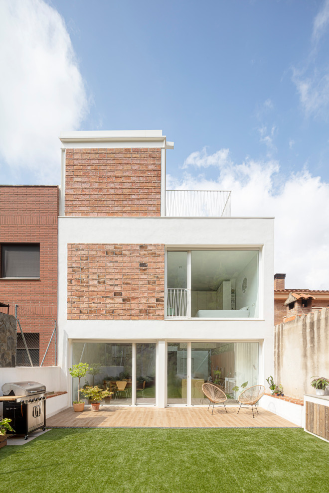 This is an example of a mid-sized contemporary three-storey white townhouse exterior in Other with mixed siding, a flat roof and a mixed roof.