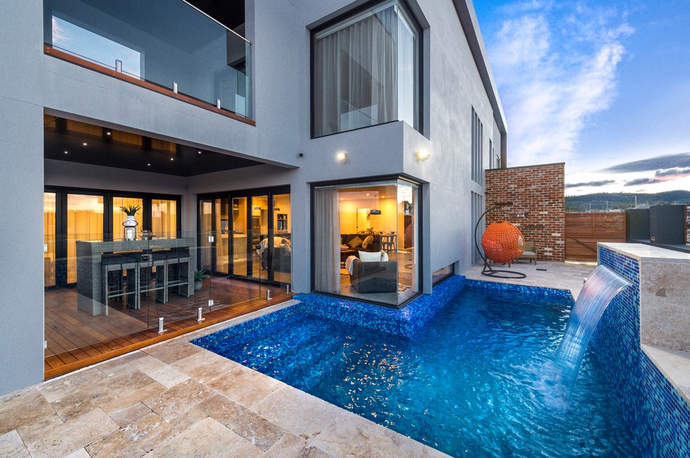 This is an example of a contemporary backyard l-shaped pool in Melbourne with a water feature and natural stone pavers.