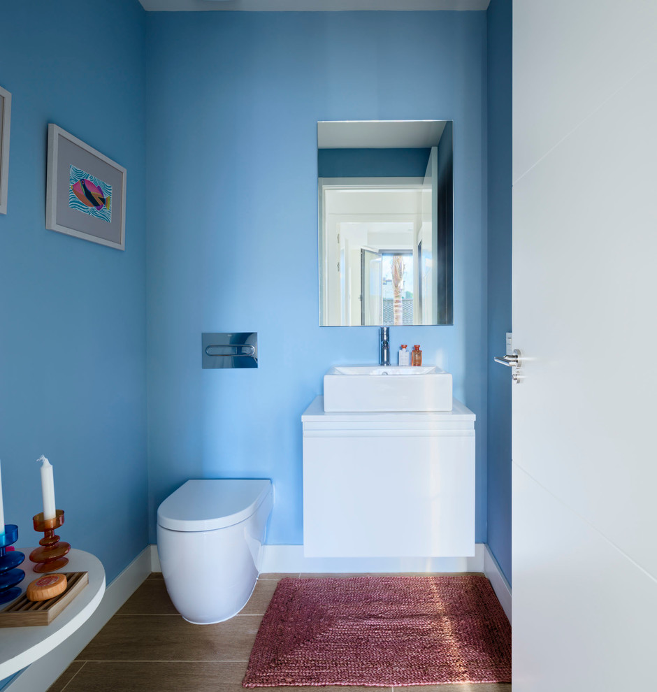 Small contemporary powder room in Malaga with flat-panel cabinets, white cabinets, a one-piece toilet, blue walls, ceramic floors and a vessel sink.