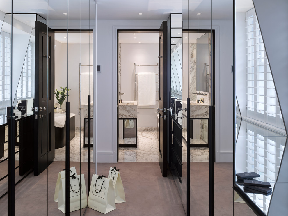 This is an example of a mid-sized transitional gender-neutral dressing room in London with glass-front cabinets and carpet.