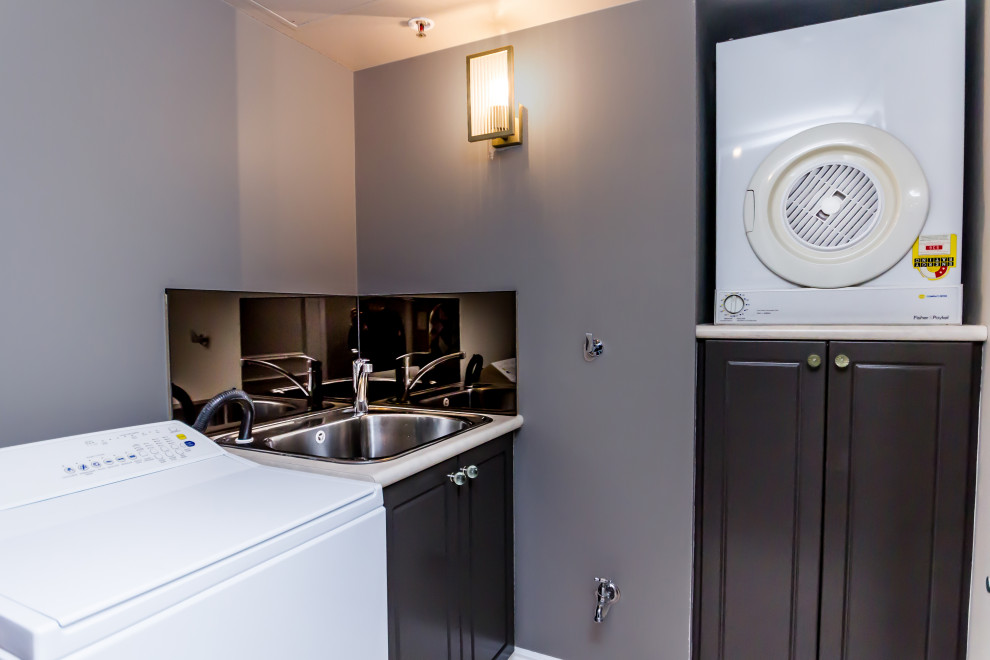 This is an example of a small transitional dedicated laundry room in Brisbane with a drop-in sink, recessed-panel cabinets, brown cabinets, laminate benchtops, brown splashback, mirror splashback, beige walls, a side-by-side washer and dryer and white benchtop.