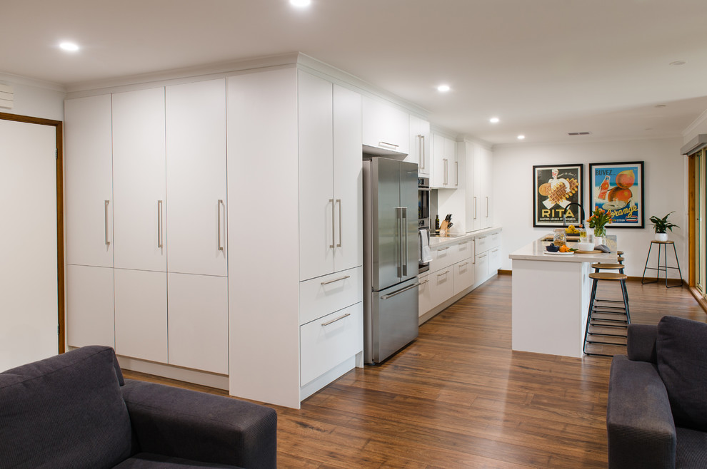 Large modern u-shaped kitchen pantry in Melbourne with a double-bowl sink, open cabinets, white cabinets, quartz benchtops, metallic splashback, glass sheet splashback, stainless steel appliances, medium hardwood floors, with island and beige benchtop.