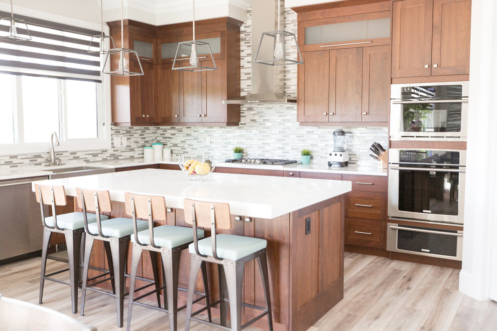 Transitional l-shaped beige floor open concept kitchen photo with a farmhouse sink, recessed-panel cabinets, medium tone wood cabinets, gray backsplash, mosaic tile backsplash, stainless steel appliances and an island