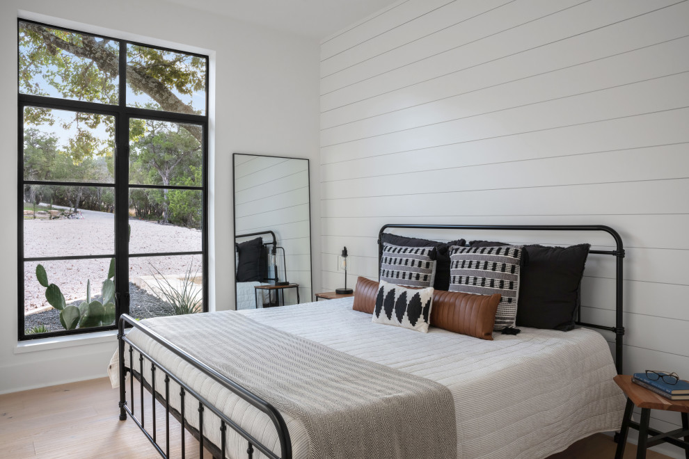 Photo of a small country guest bedroom in Austin with white walls, light hardwood floors, brown floor and planked wall panelling.