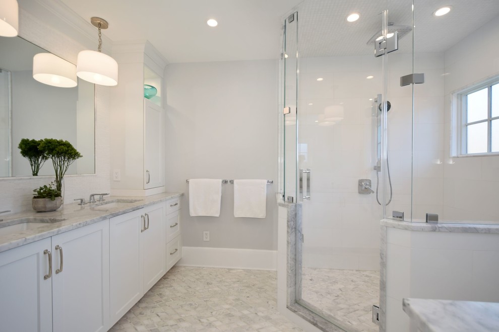 Photo of a mid-sized transitional master bathroom in New York with shaker cabinets, white cabinets, a corner shower, white tile, porcelain tile, grey walls, porcelain floors, an undermount sink, marble benchtops, white floor, a hinged shower door and grey benchtops.