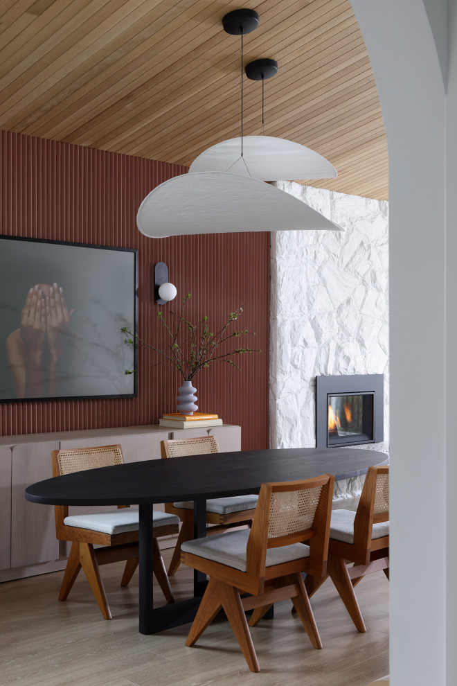 Midcentury dining room in Vancouver with red walls, laminate floors, a standard fireplace, a stone fireplace surround, exposed beam and wood walls.