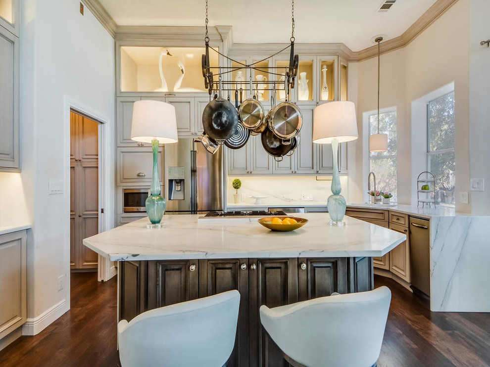 Transitional l-shaped open plan kitchen in Austin with raised-panel cabinets, distressed cabinets, marble benchtops, white splashback, with island, stainless steel appliances, an undermount sink and medium hardwood floors.