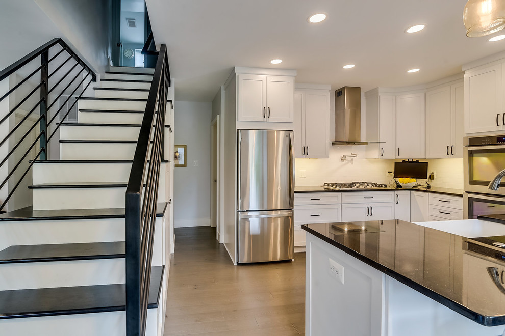 Inspiration for a transitional u-shaped light wood floor and gray floor eat-in kitchen remodel in DC Metro with a farmhouse sink, shaker cabinets, white cabinets, granite countertops, white backsplash, ceramic backsplash, stainless steel appliances, no island and black countertops