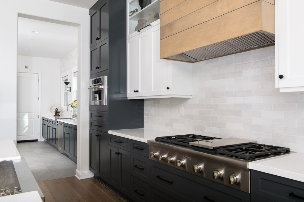 Kitchen - transitional kitchen idea in Orange County with a farmhouse sink, shaker cabinets, white cabinets, quartzite countertops, white backsplash, subway tile backsplash, stainless steel appliances, an island and white countertops