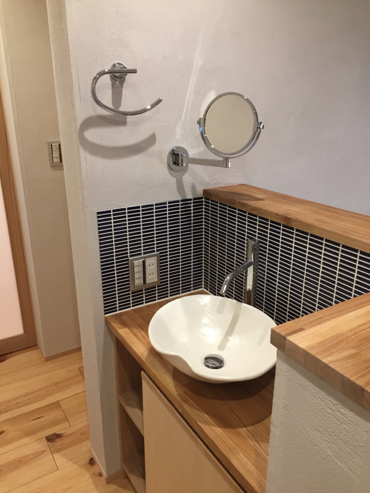 Photo of a mid-sized scandinavian powder room in Other with light wood cabinets, blue tile, white walls, light hardwood floors, a vessel sink, wood benchtops, a built-in vanity and wood.