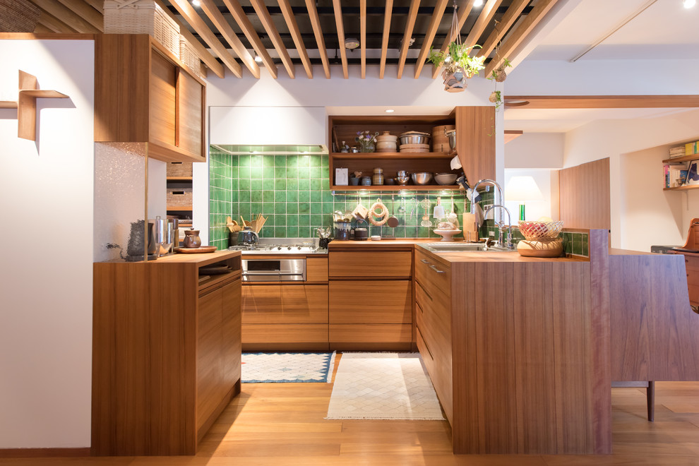 Photo of a scandinavian l-shaped open plan kitchen with a single-bowl sink, flat-panel cabinets, medium wood cabinets, wood benchtops, green splashback, medium hardwood floors, a peninsula, brown floor and brown benchtop.