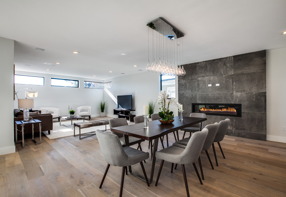 This is an example of a contemporary open plan dining in Orange County with beige walls, light hardwood floors, a ribbon fireplace and a metal fireplace surround.